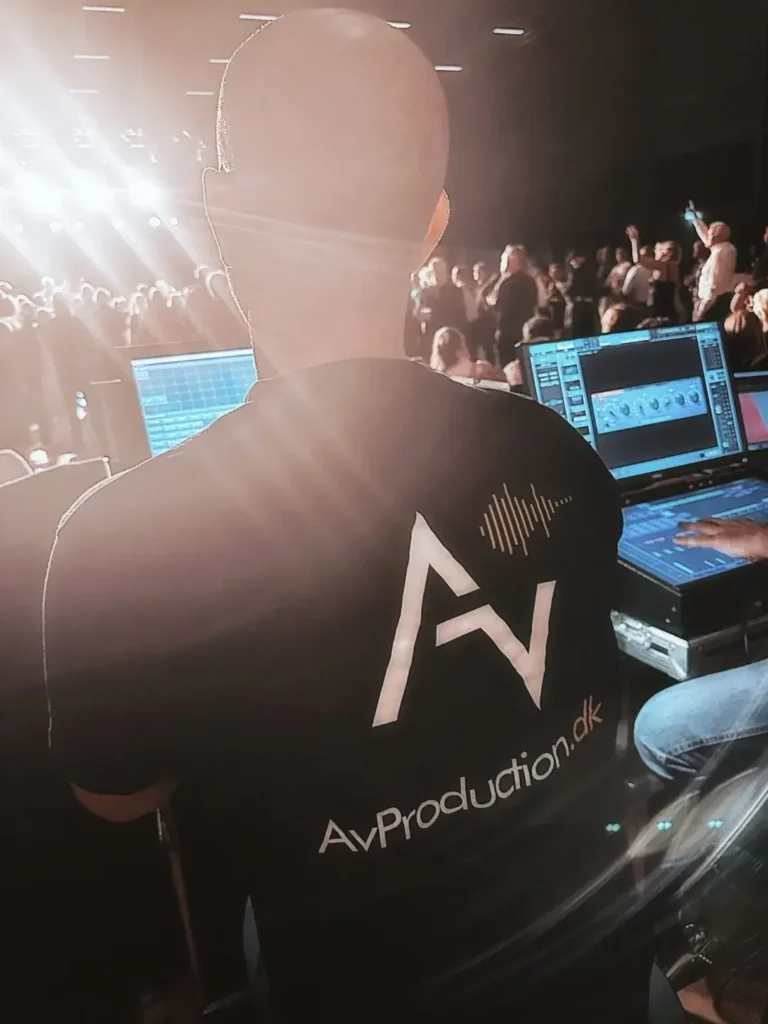 En person i sort t-shirt med AvProduction.dk logo arbejder bag scenen.